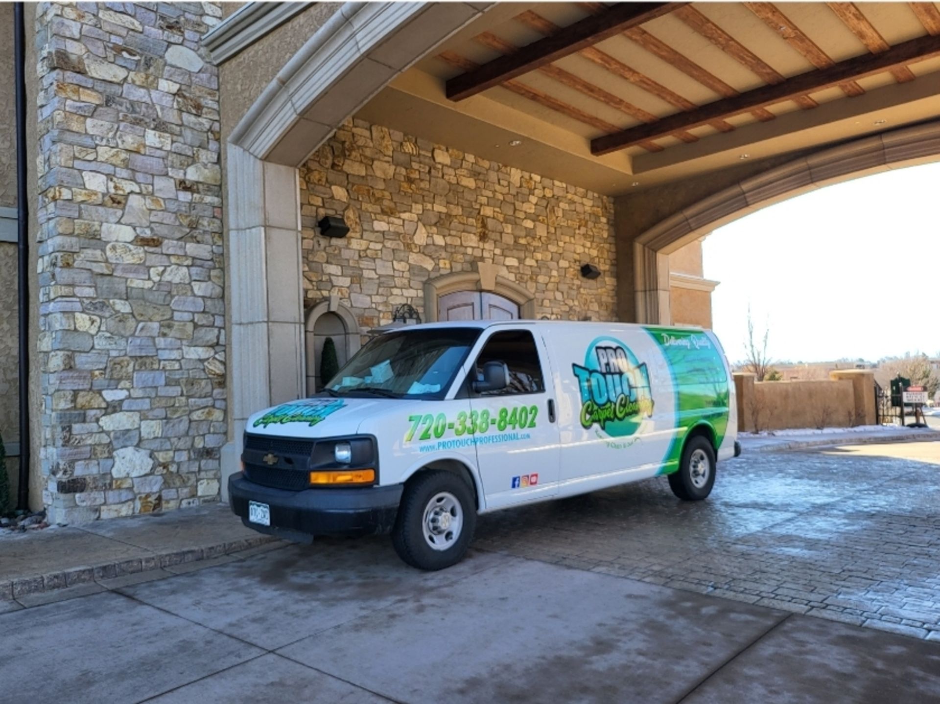 A white van is parked in front of a stone building.