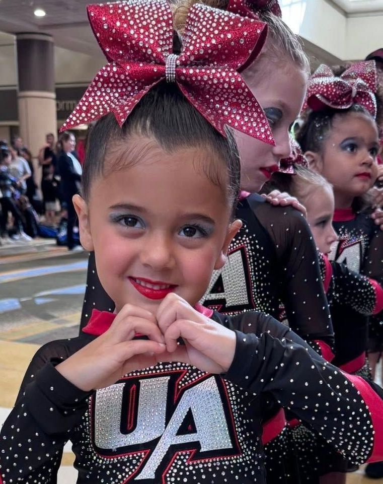 A cheerleader wearing a ua uniform is making a heart shape with her hands
