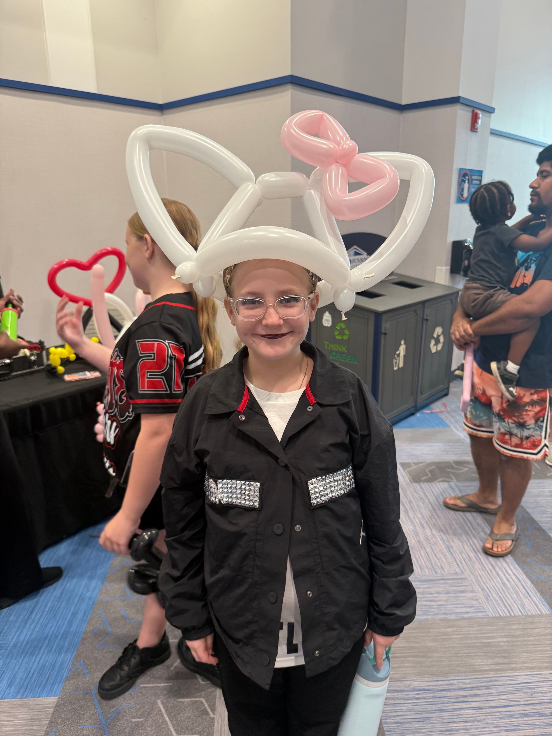 A girl wearing a hat made of balloons is holding cotton candy.