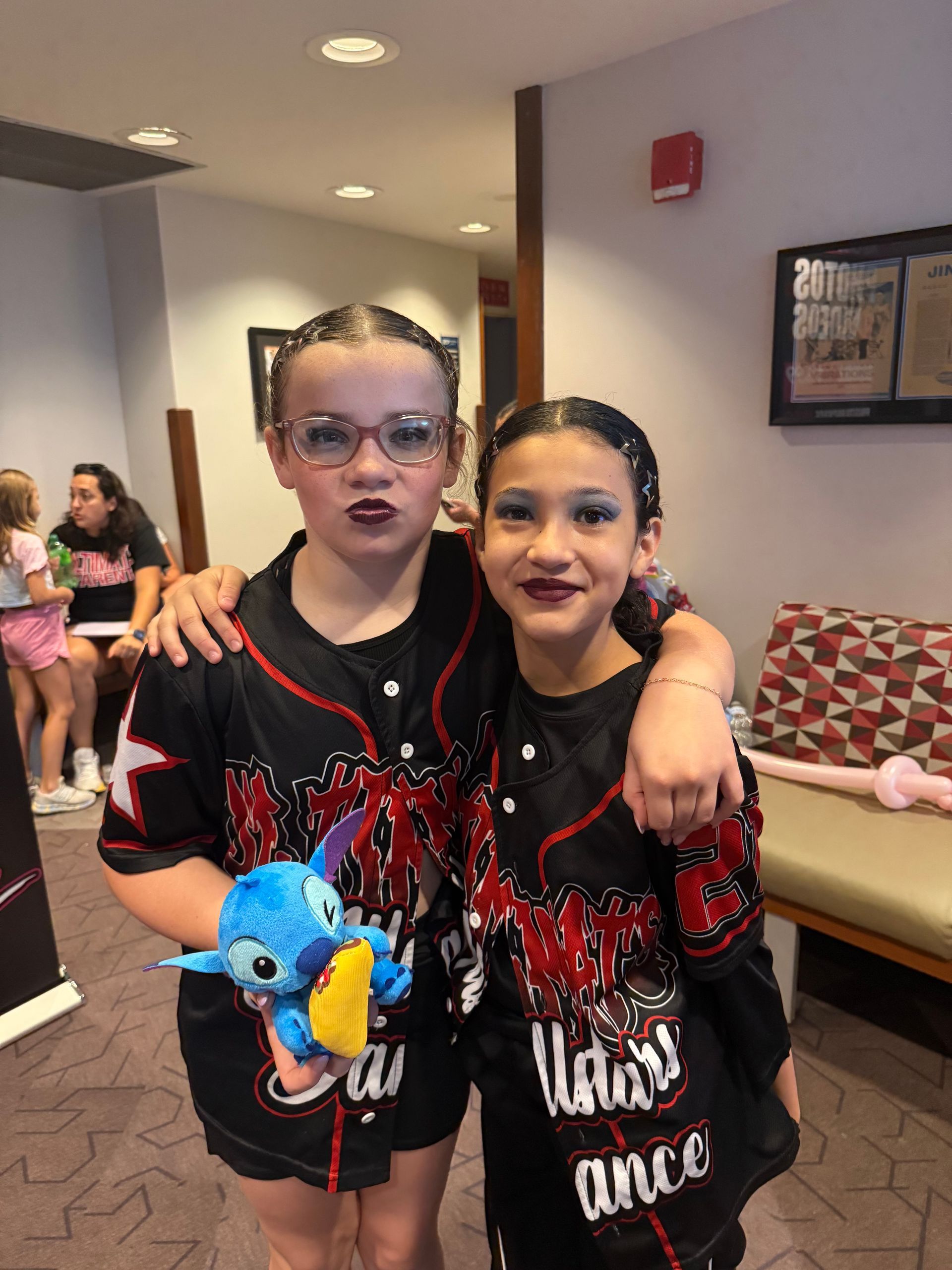 Two young girls are posing for a picture and one of them is holding a stuffed animal.