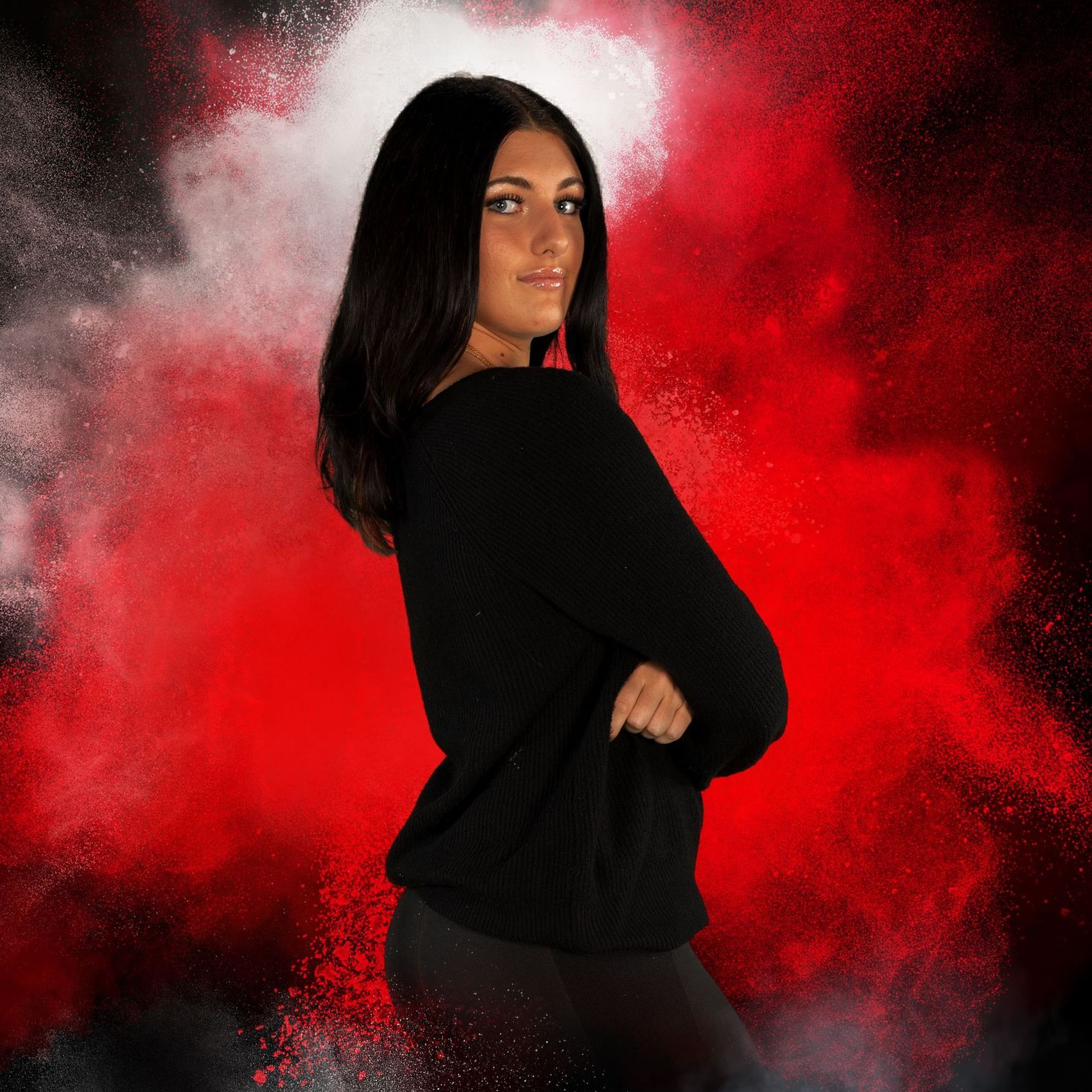 A woman in a black sweater is standing in front of a red background.