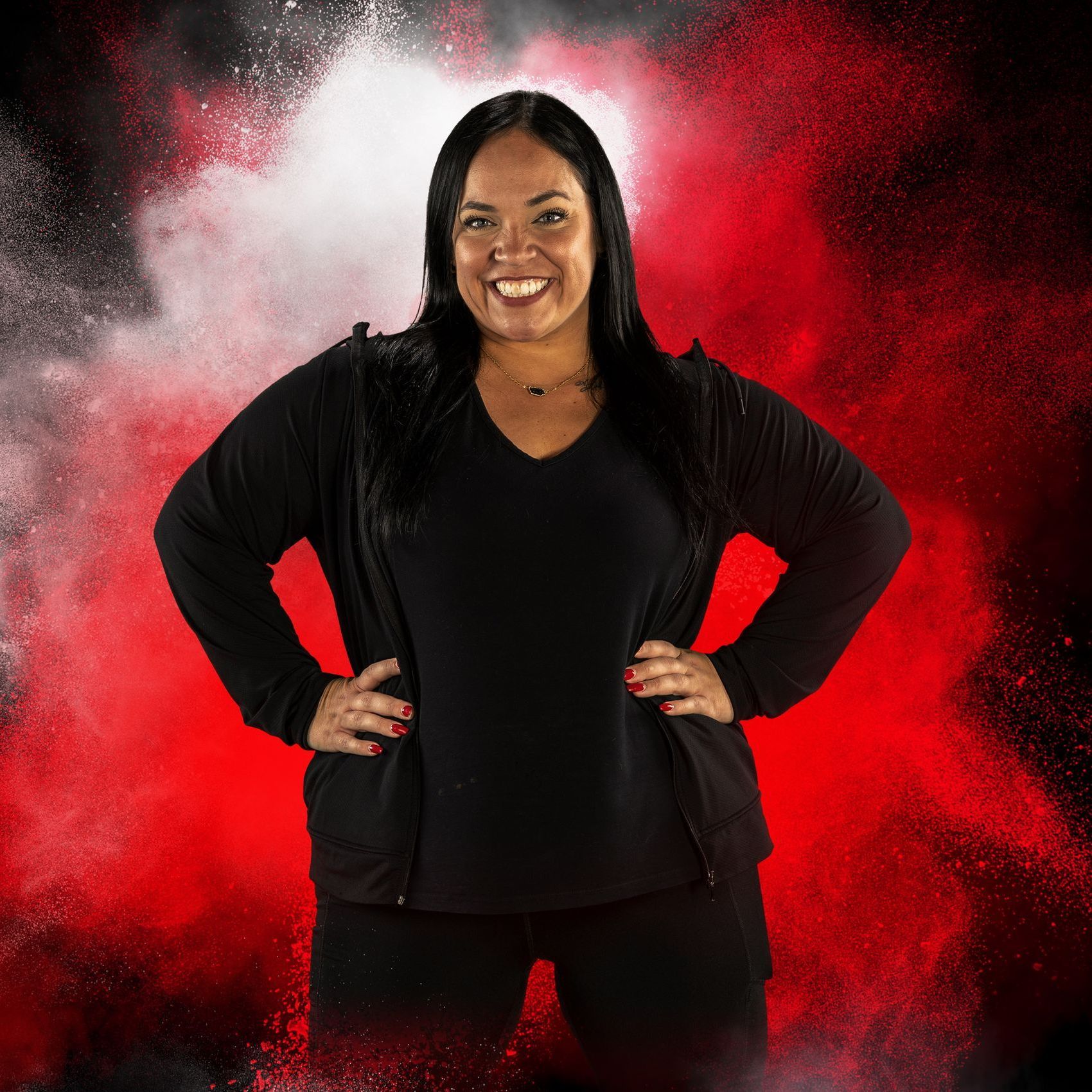 A woman is standing with her hands on her hips in front of a red background.