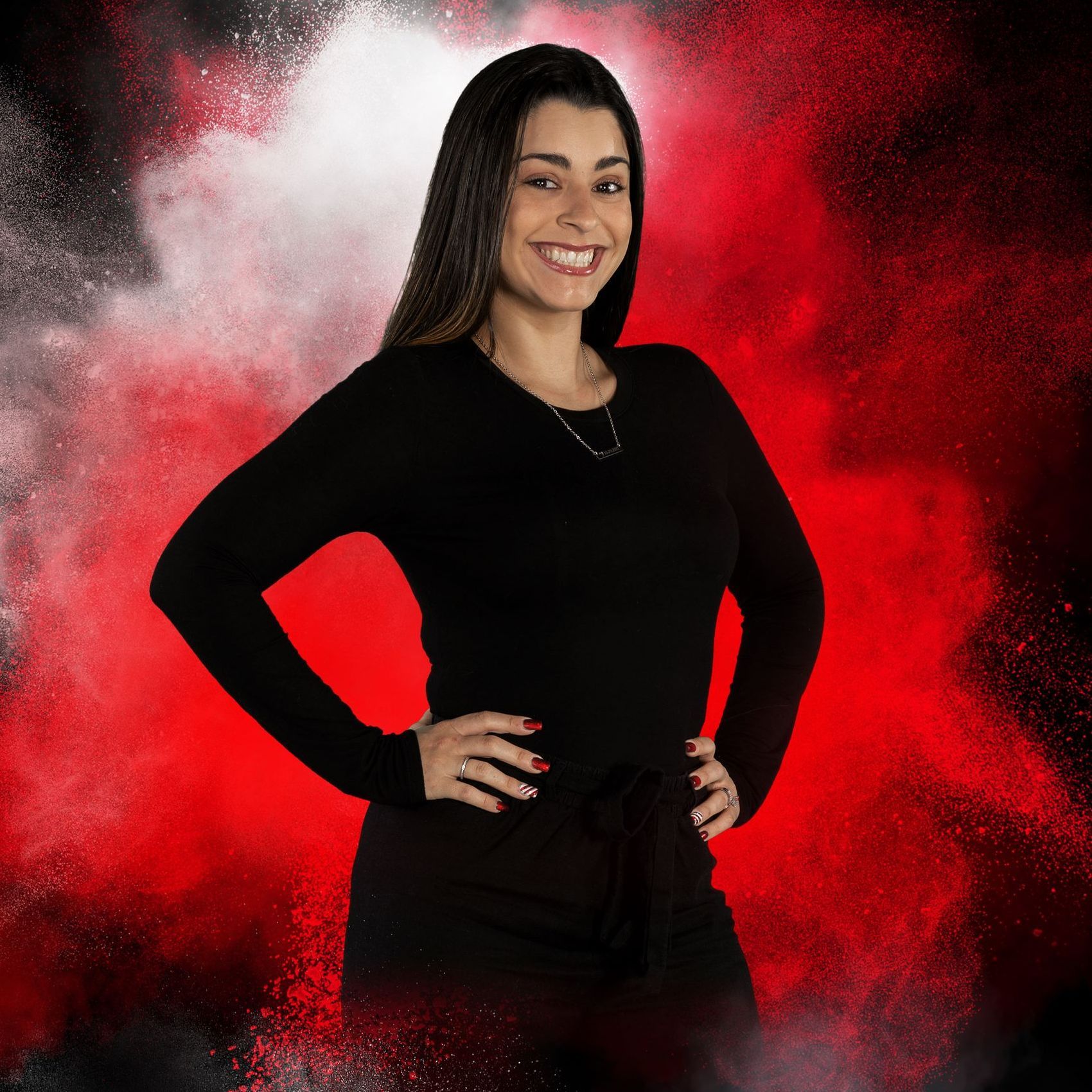 A woman in a black shirt is standing with her hands on her hips in front of a red background.
