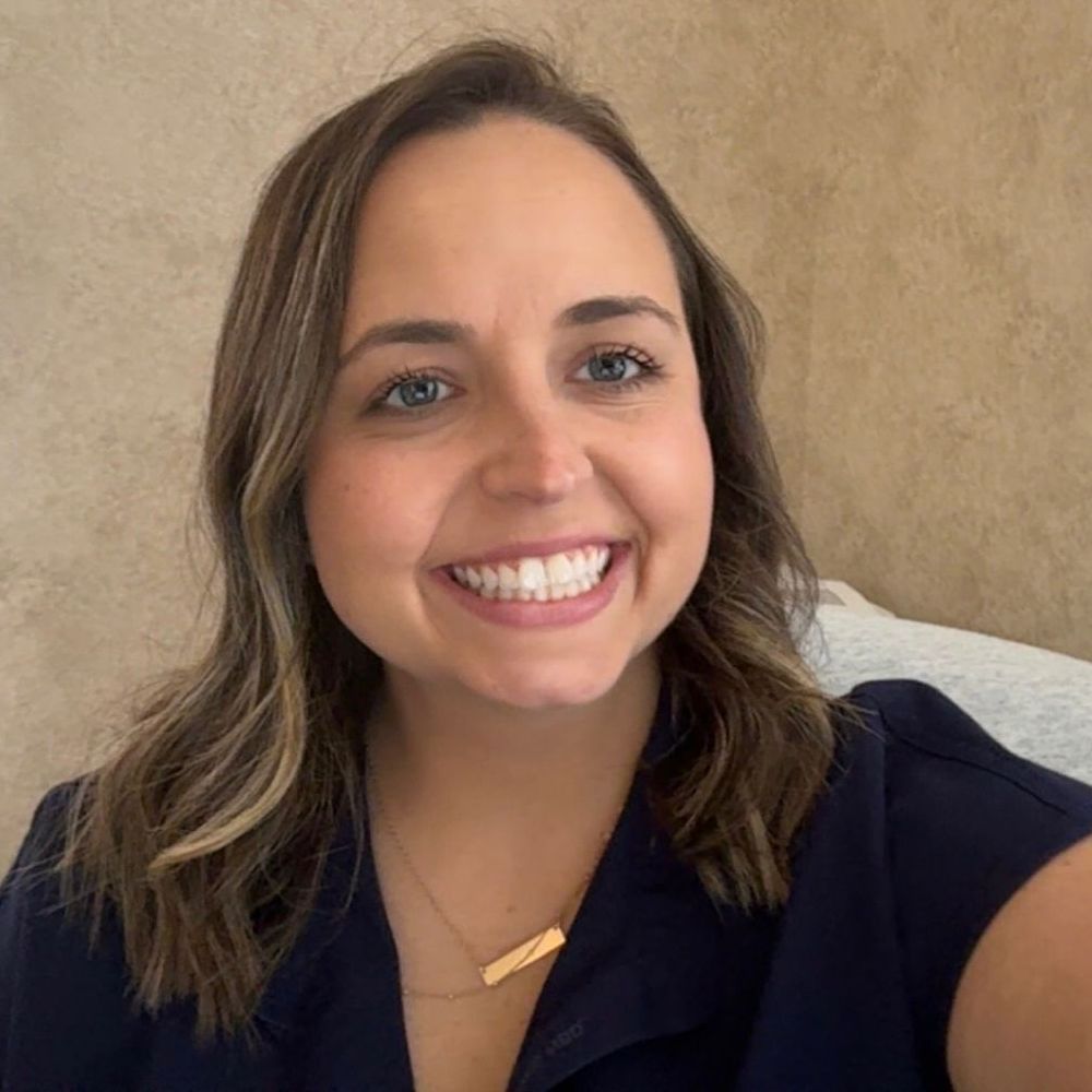 A woman wearing a blue shirt and a gold necklace is smiling for the camera.