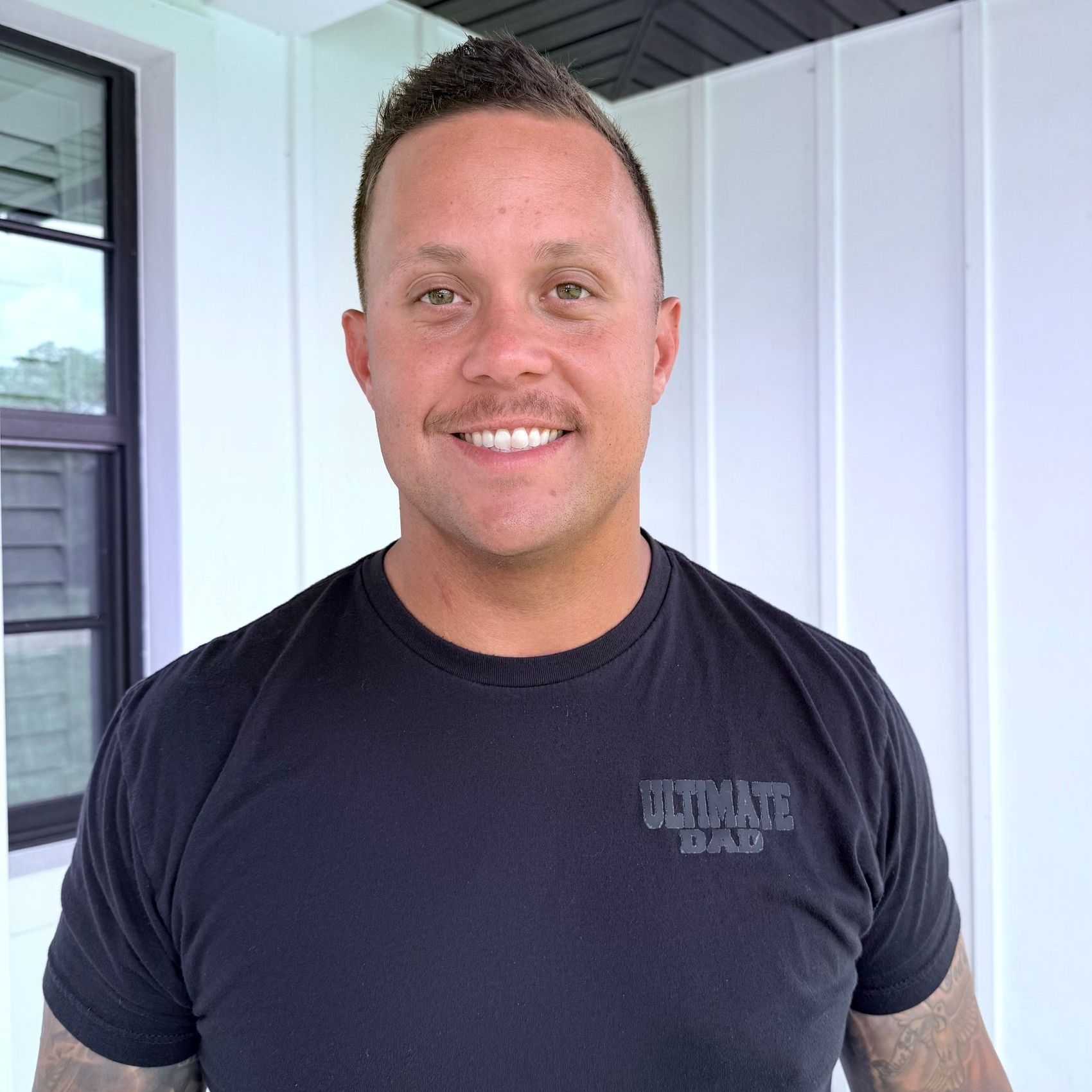 A man wearing a black t-shirt is smiling for the camera.