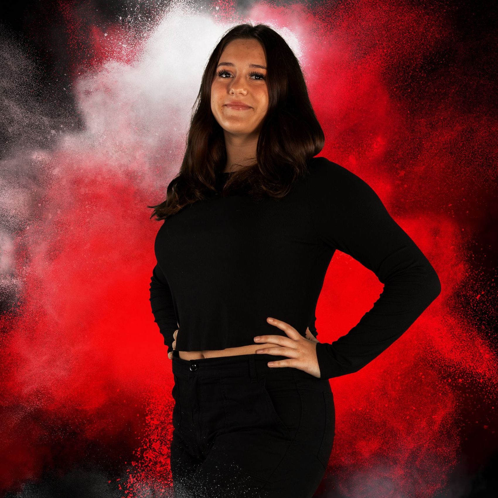 A woman is standing with her hands on her hips in front of a red background.