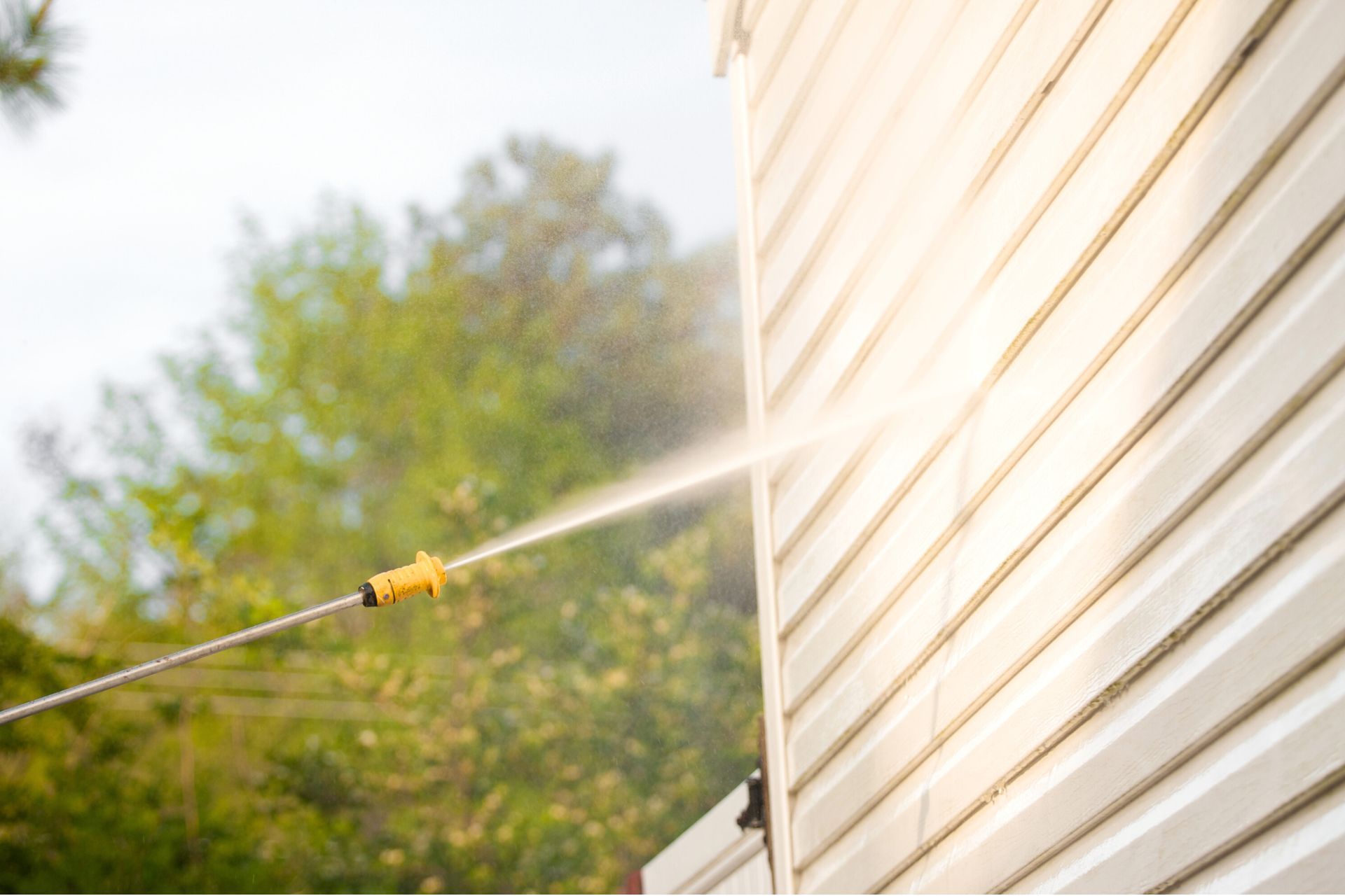A person is using a high pressure washer to clean the side of a house.