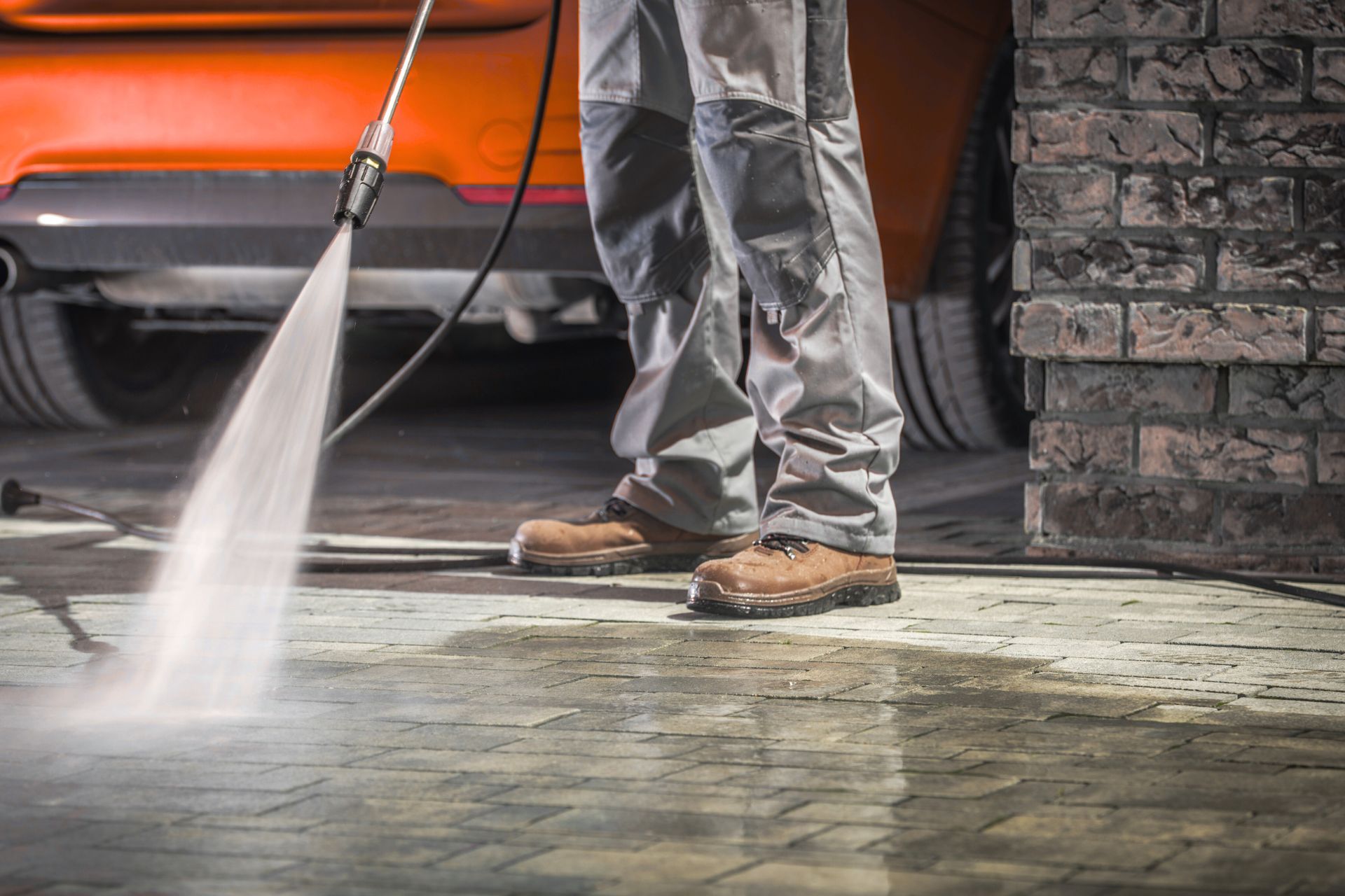A man is using a high pressure washer to clean a driveway.