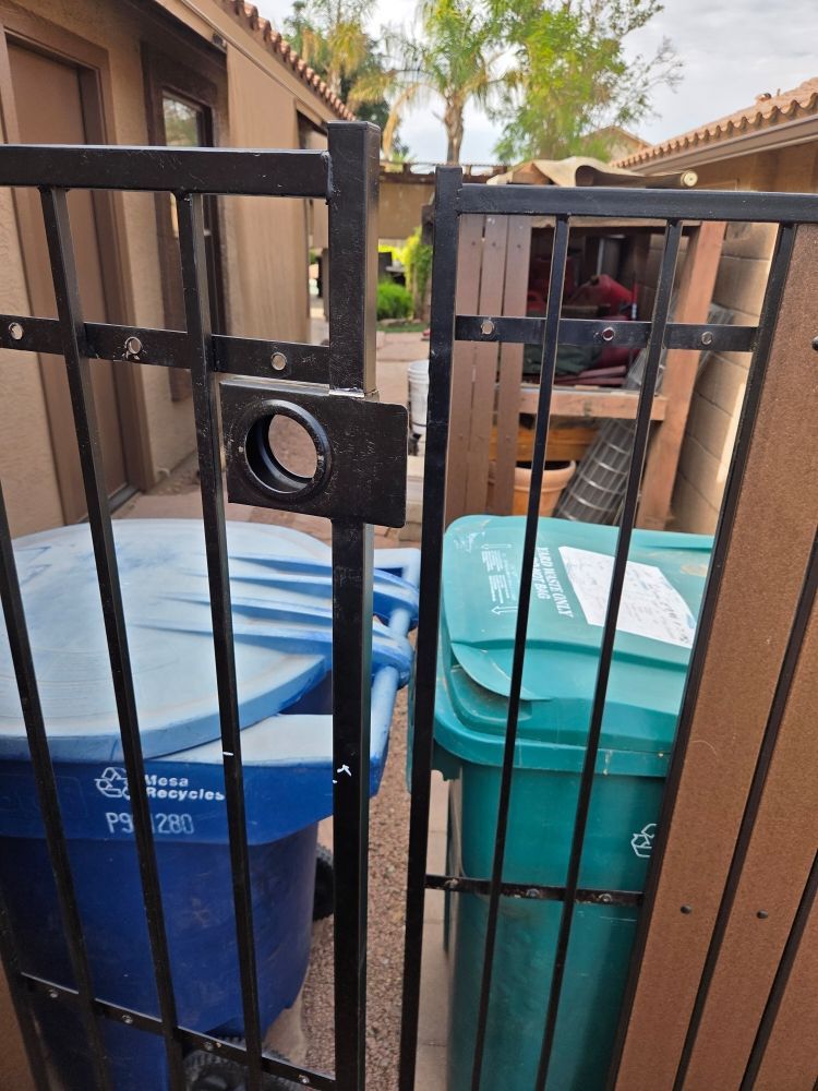 Black metal gate with a lock, partially blocking two trash bins.