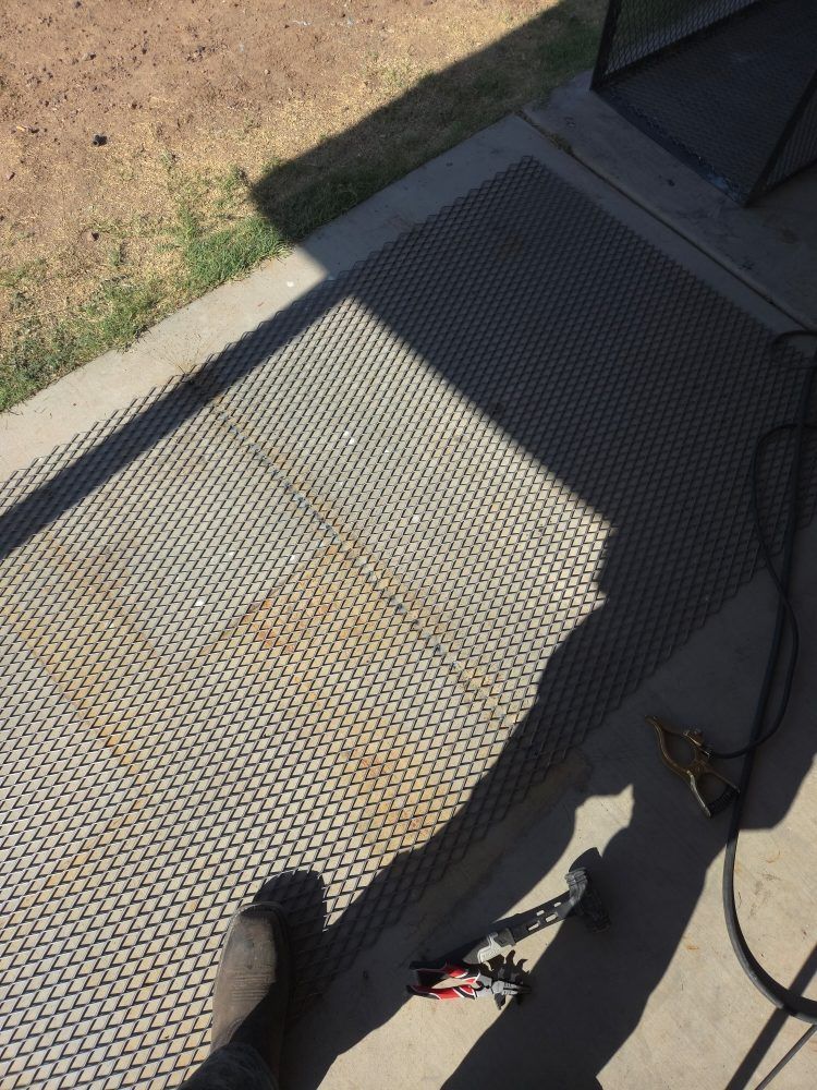 Black mesh mat on concrete patio; grass and tools visible.