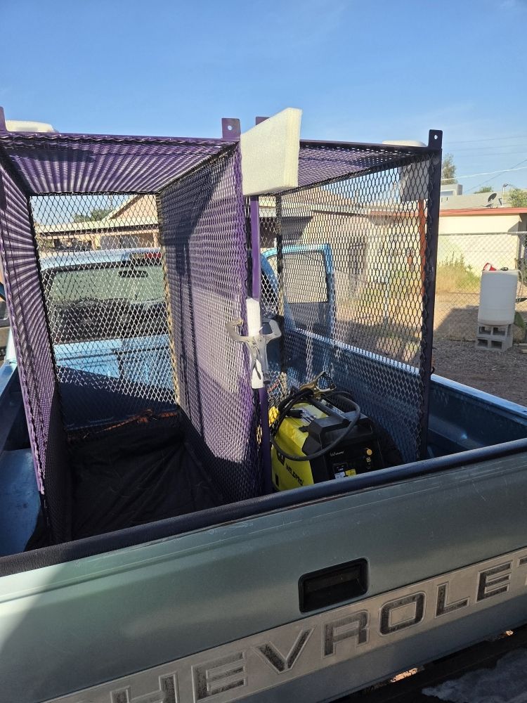 Purple-caged truck bed holding equipment; a small engine and garbage bag visible. Sunlight, outdoors.