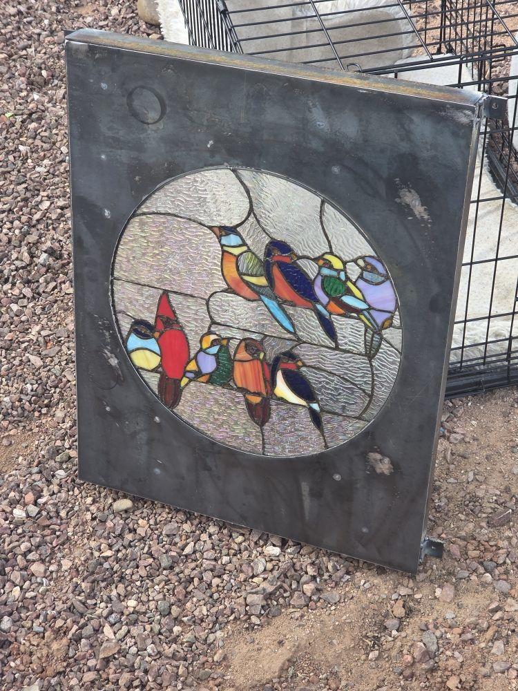 Stained glass panel with colorful birds perched on a wire, set in a gray frame.