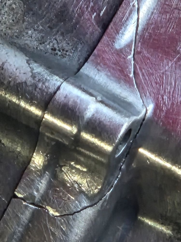 Close-up of a metal object showing cracks along weld lines and edges, with areas of shiny, polished metal.
