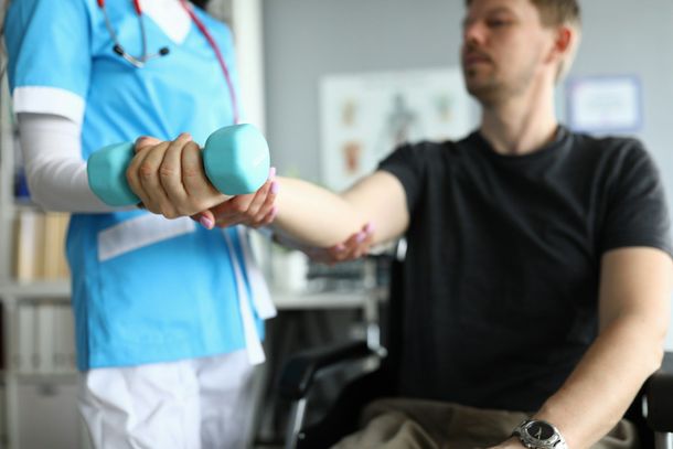 Medical professional assists a patient with a dumbbell exercise in a doctor's office.