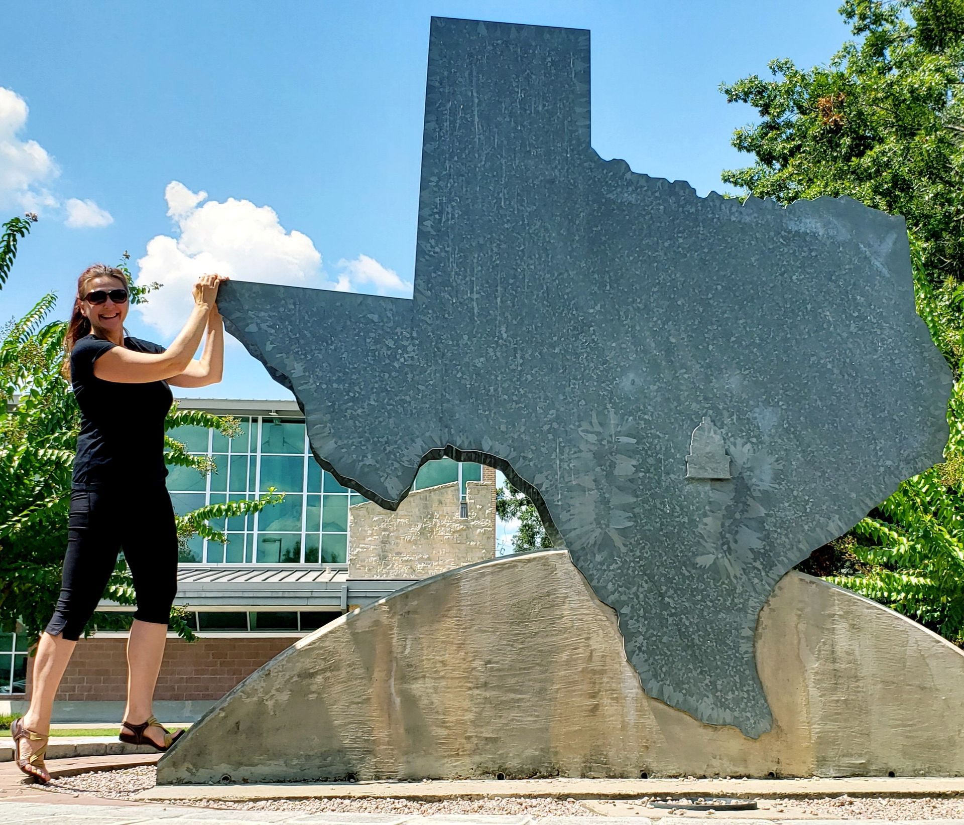 Woman pushing a large granite sculpture of the state of Texas outside a building.