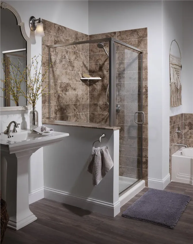 A bathroom features a stone-tiled walk-in shower, a pedestal sink, and a gray rug on dark wooden flooring.
