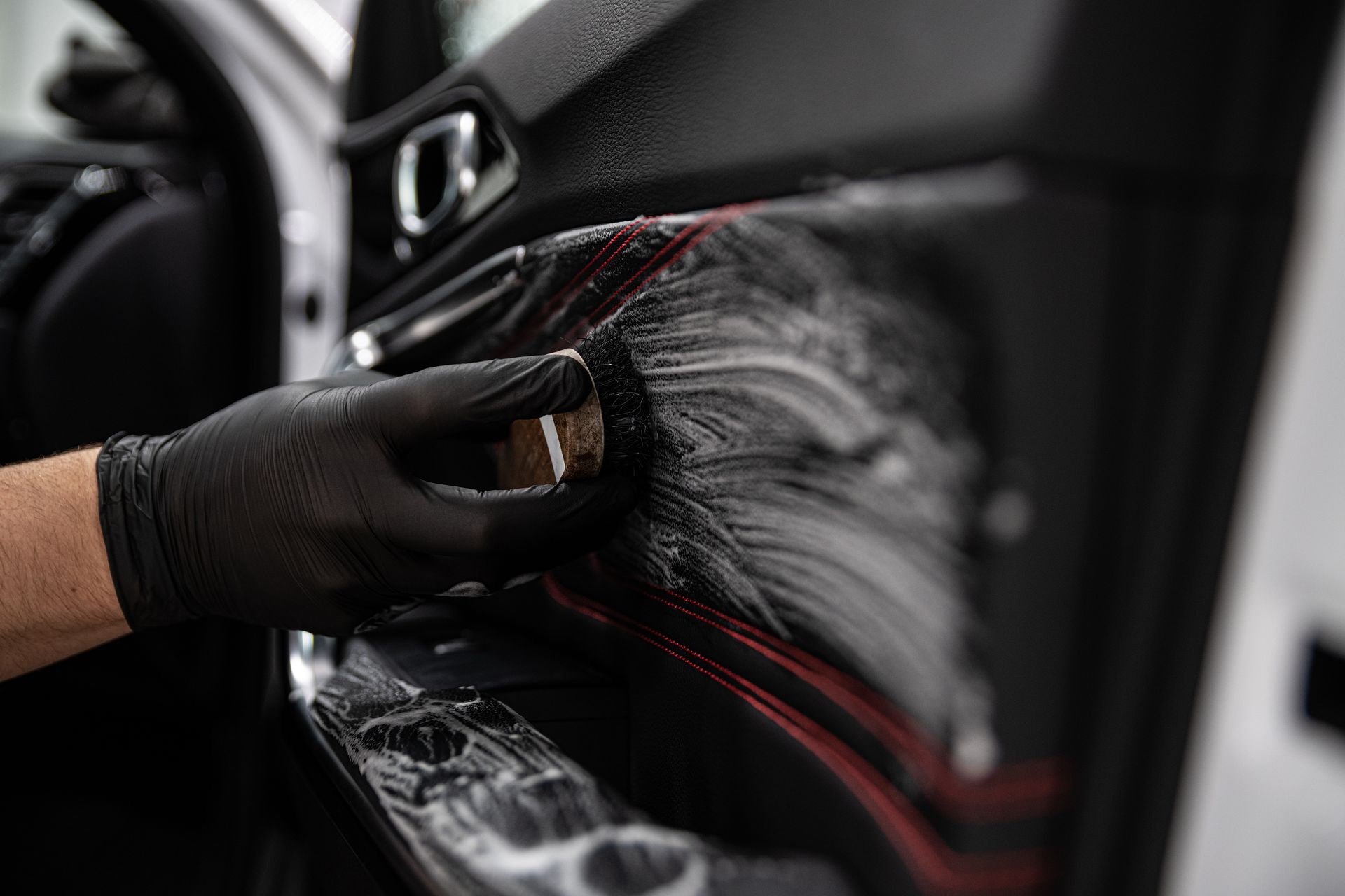 Gloved hand applying black cleaner to a car door interior with a cloth.