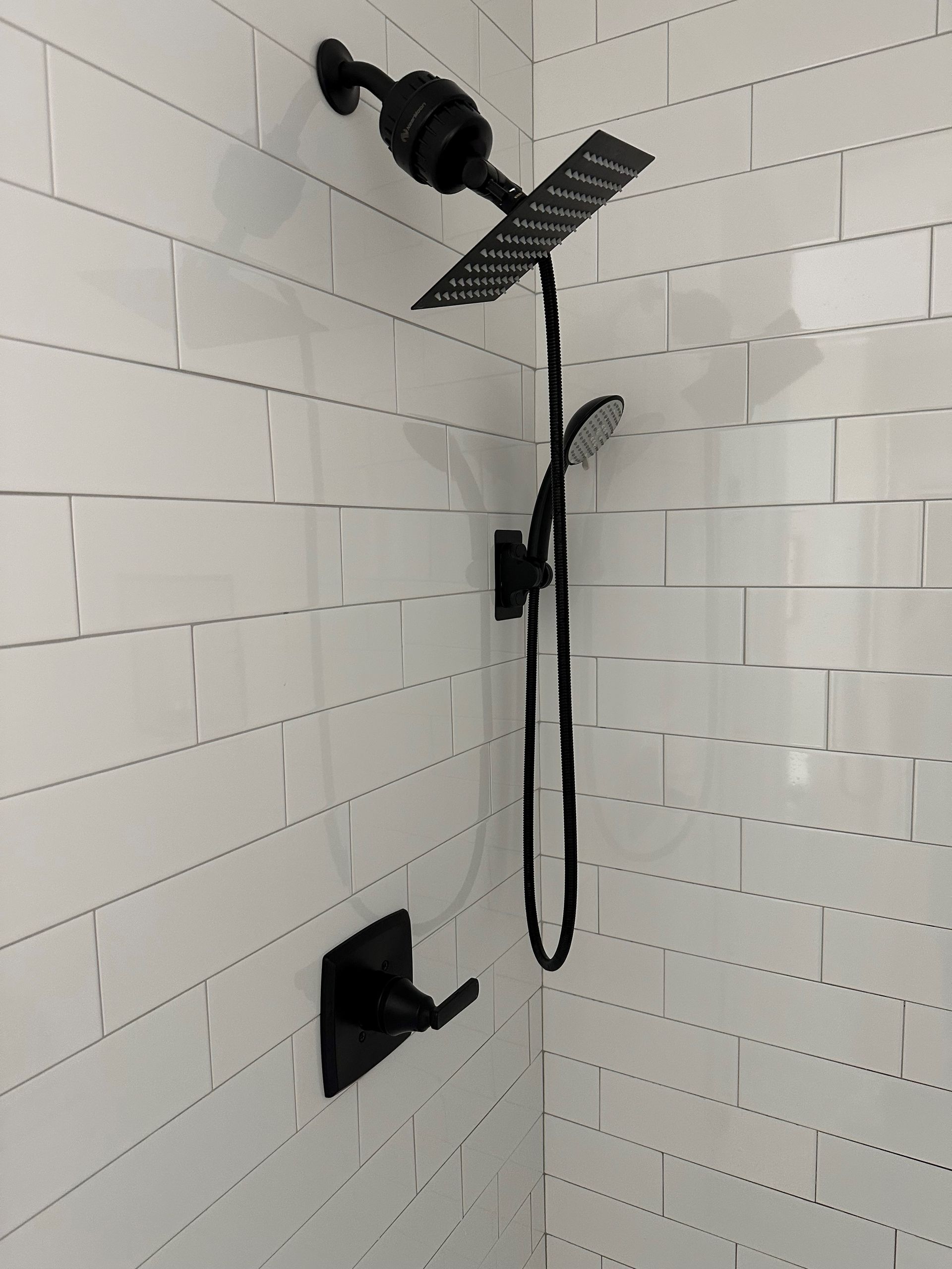 A shower with white tiles and a black shower head  - Hendersonville, TN - Chris' Plumbing Service & Repair
