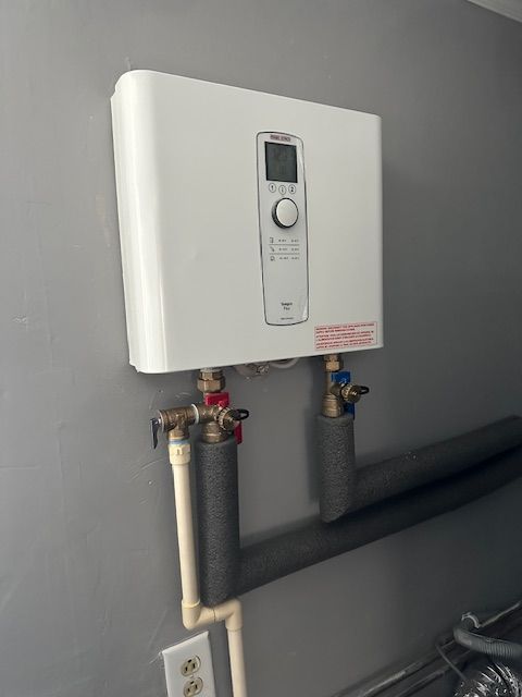 A white water heater is hanging on a wall next to pipes.