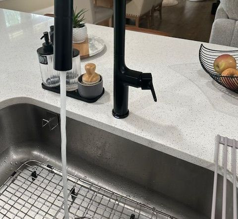 A kitchen sink with water running from a black faucet.