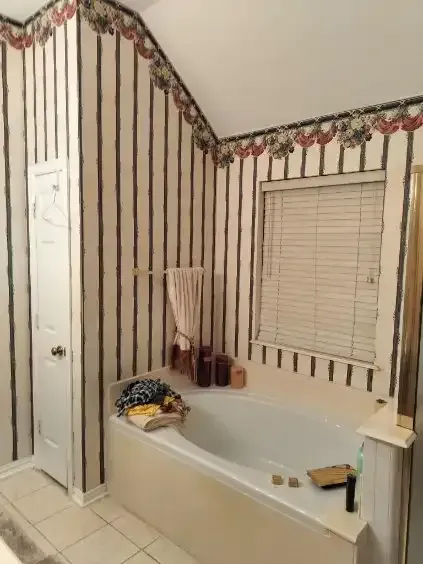 Bathroom with striped wallpaper, a bathtub, a window with blinds, and a white door.