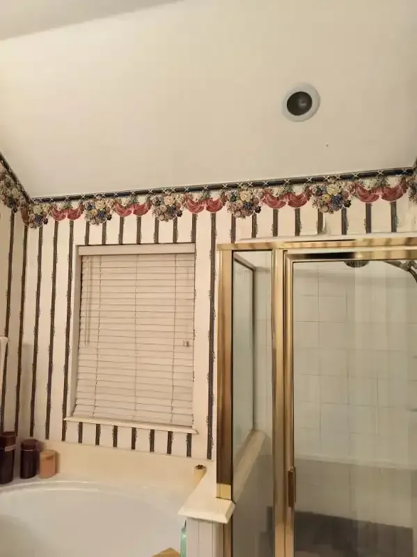 Bathroom with striped wallpaper, floral border, gold shower frame, and blinds.