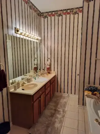 Bathroom with striped wallpaper, double vanity, mirror, and a light fixture above it.