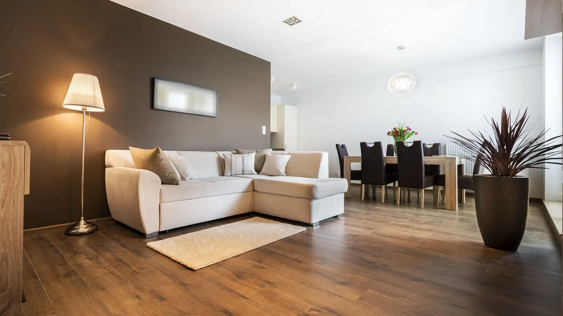Living room with light-colored sectional sofa, dark brown accent wall, and dining area.