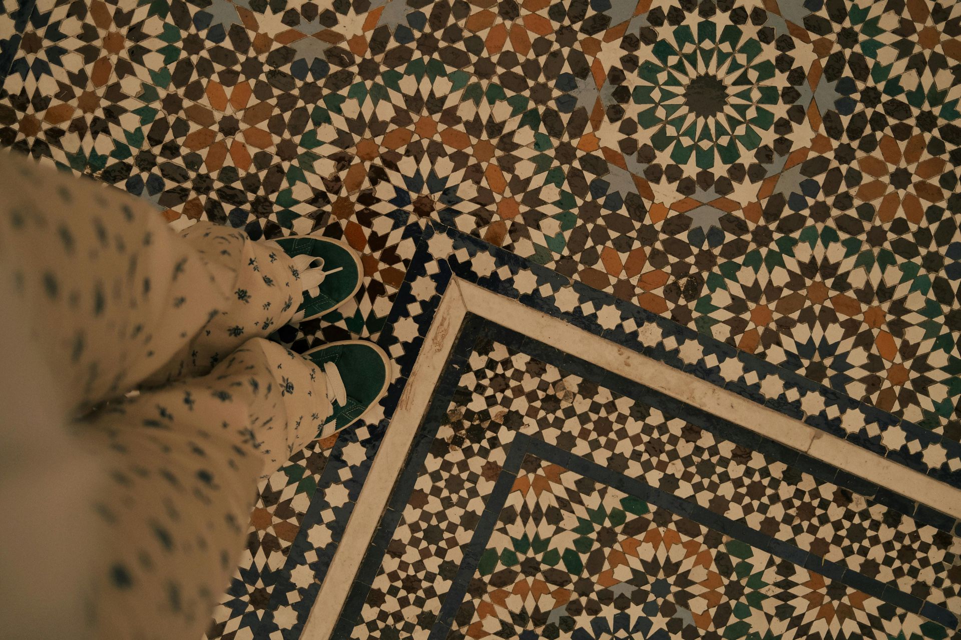 Person standing on intricate tile floor. Green shoes. Brown, blue, and white geometric patterns.