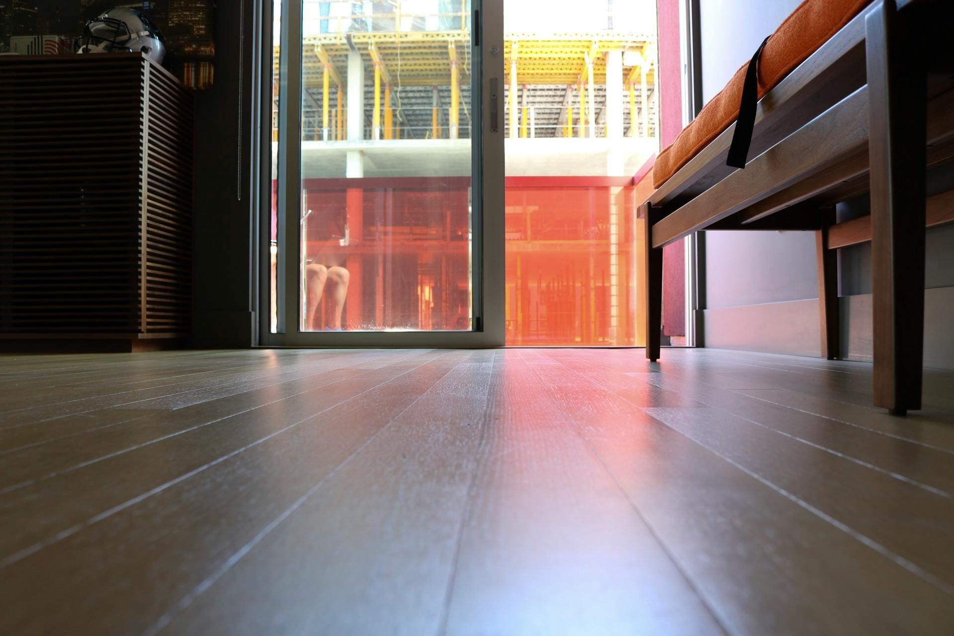 Low-angle view of wood floor, glass door with red panel, and bench with orange cushion.