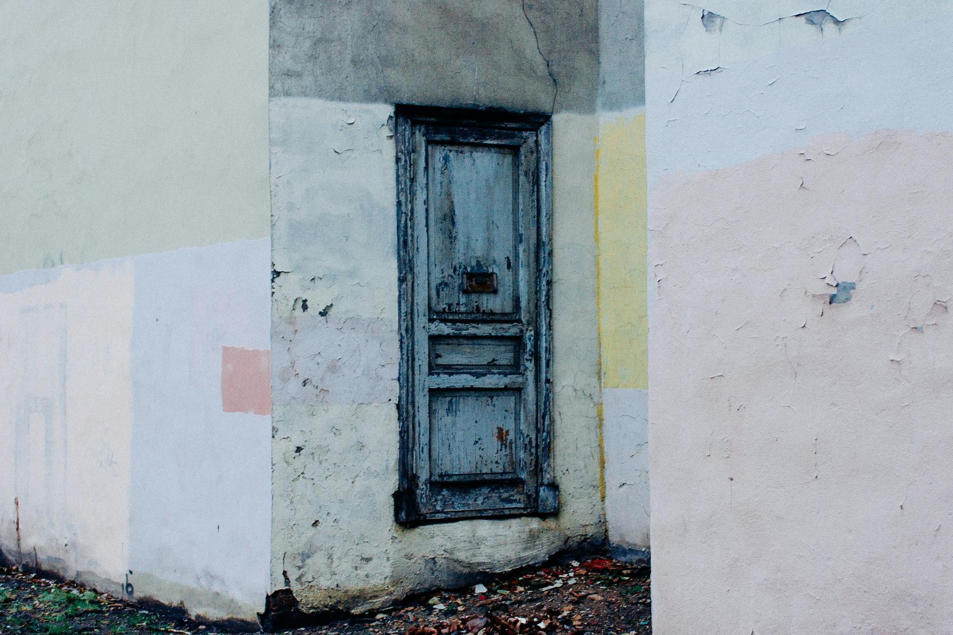 Old weathered blue door set into a multi-colored stucco building.