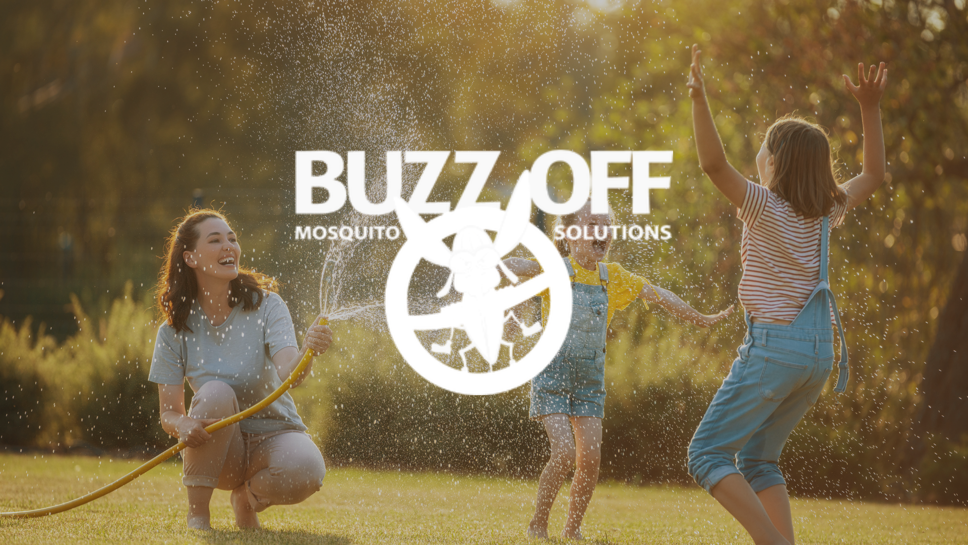 A woman and two children are playing in the grass with a hose.