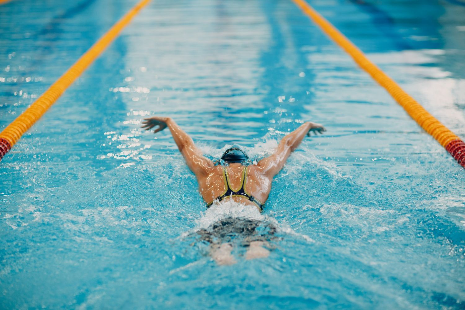 A woman is swimming in a swimming pool with her arms outstretched.
