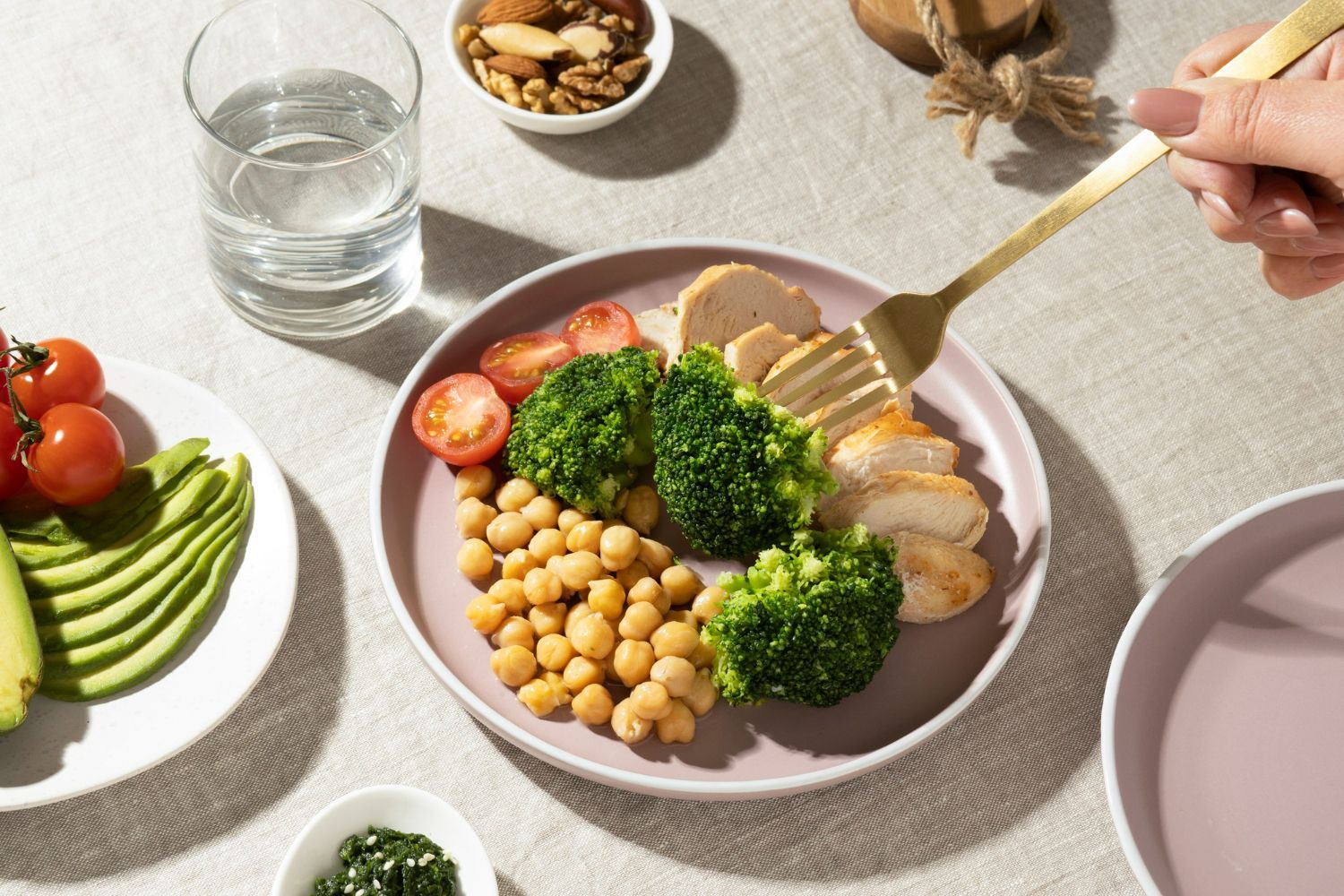 A person is eating a plate of food with broccoli , chickpeas , tomatoes and avocado.