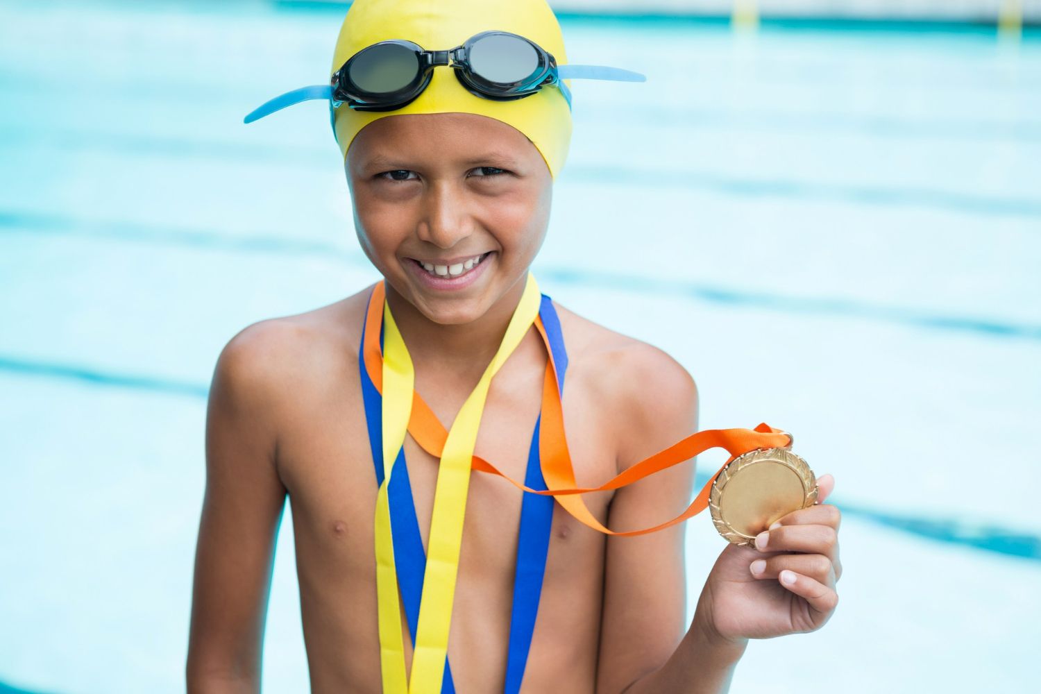 A young boy is holding a gold medal in front of a swimming pool.