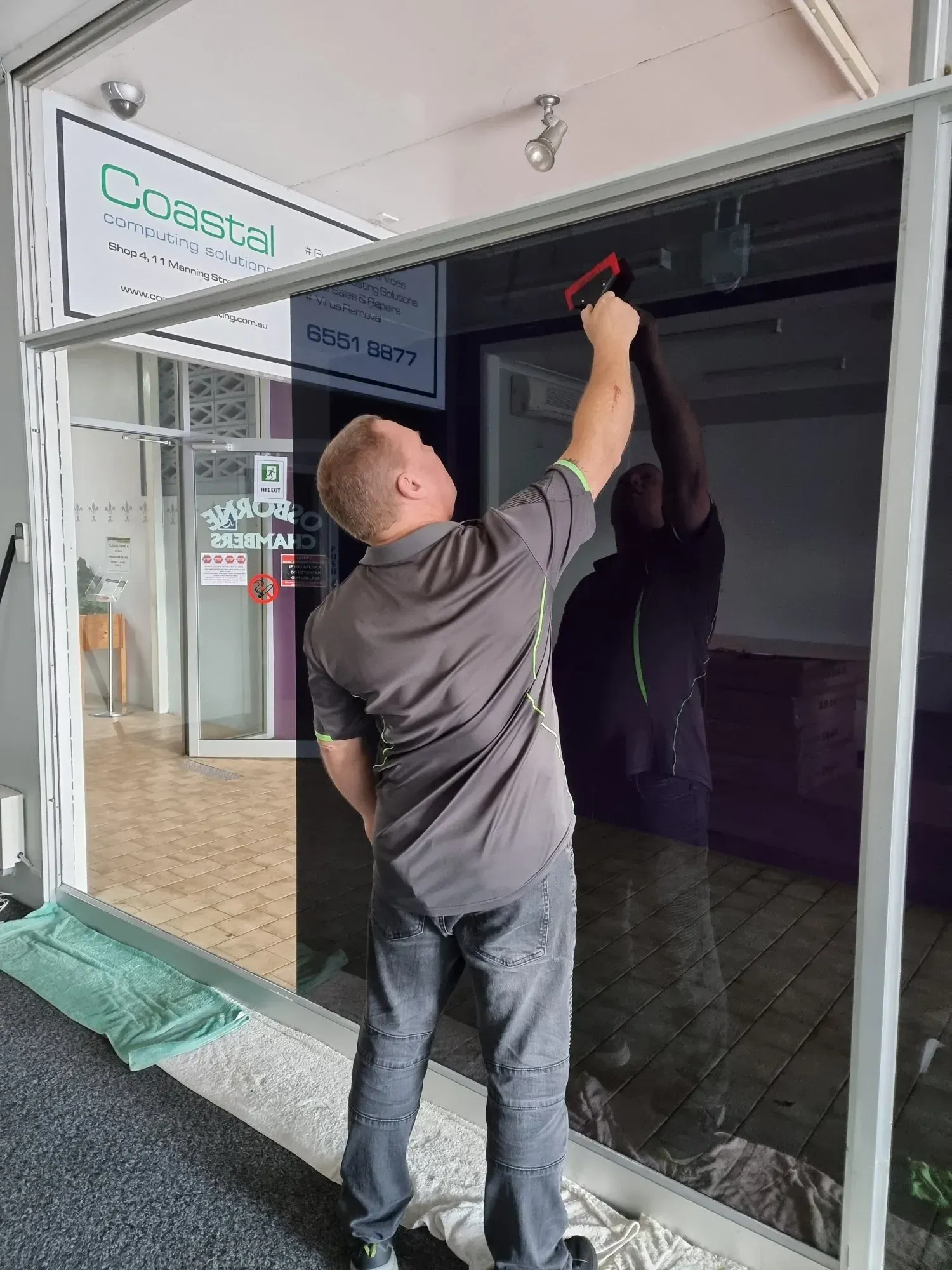 Man Applying Window Tint to a Large Glass Window, Indoors — Awesome Window Tint In Wauchope, NSW