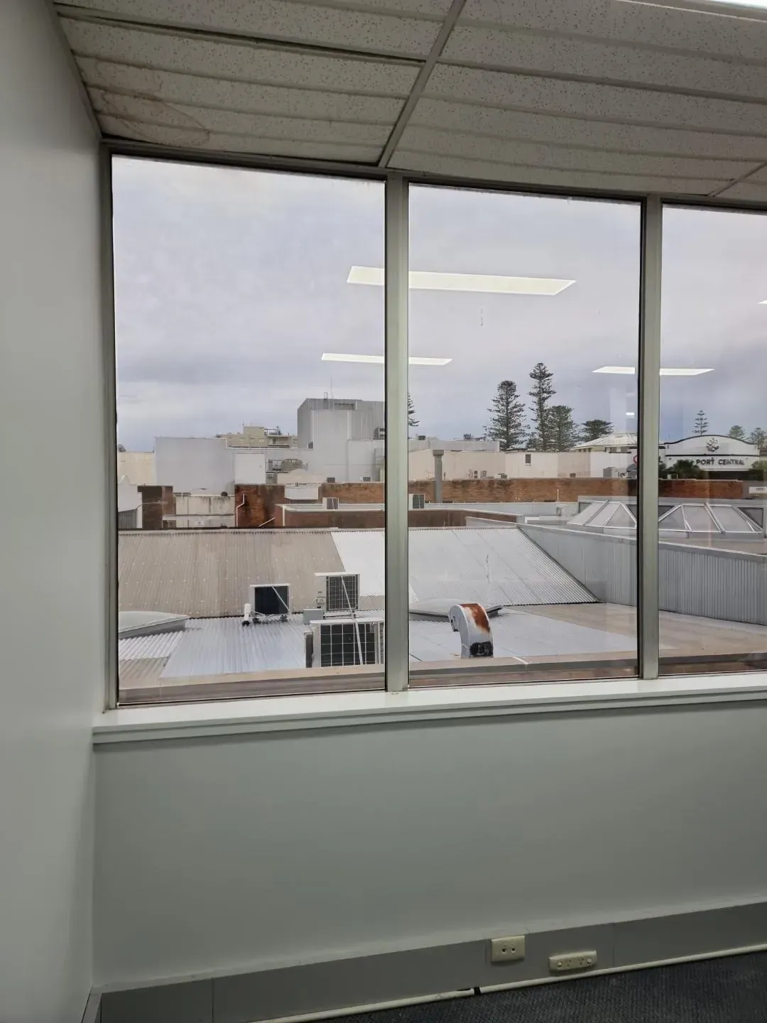 View Through an Office Window Overlooking Rooftops and a Cloudy Sky — Awesome Window Tint In Wauchope, NSW