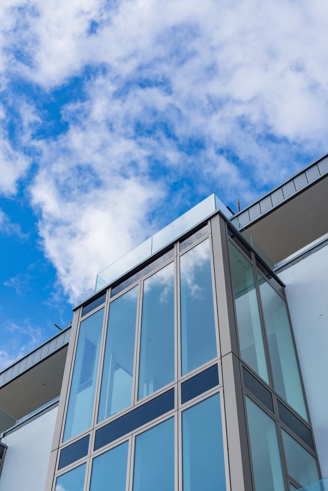 Glass-walled building section against a bright blue sky with clouds. — Awesome Window Tint In Wauchope, NSW