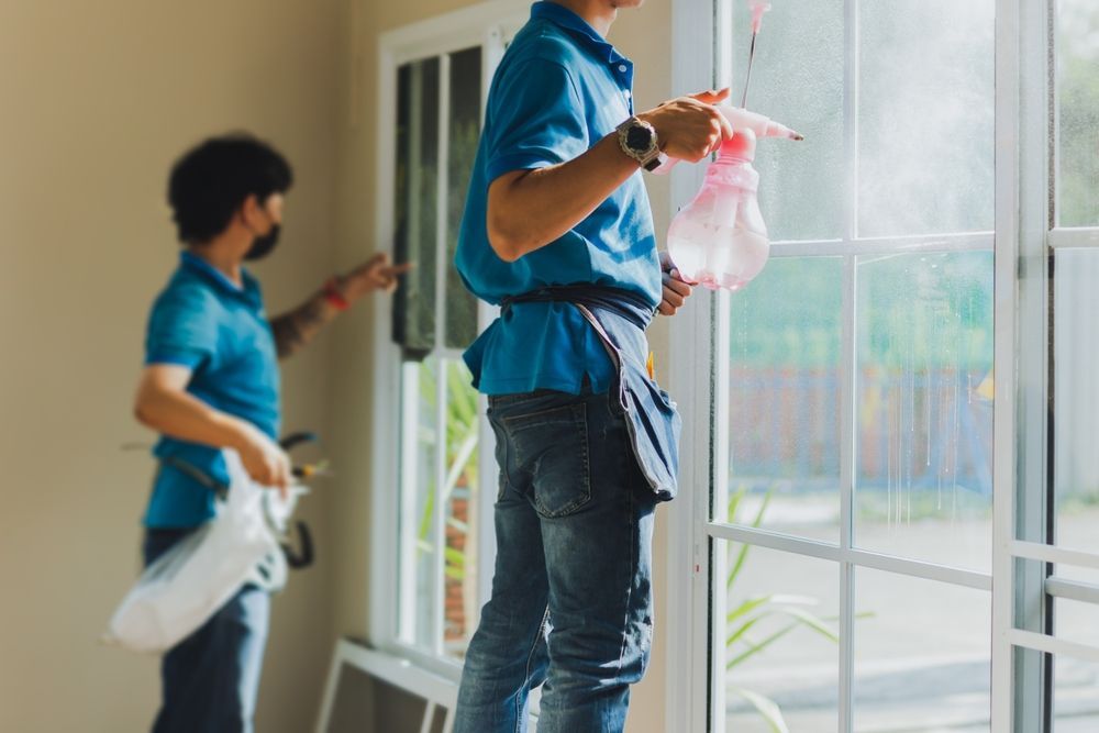 Two People Applying Tint to a Window; One Sprays — Awesome Window Tint In Kempsey, NSW