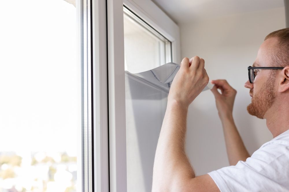 Man Applying Window Film to a White Window Frame, Outdoors Visible — Awesome Window Tint In Taree, NSW