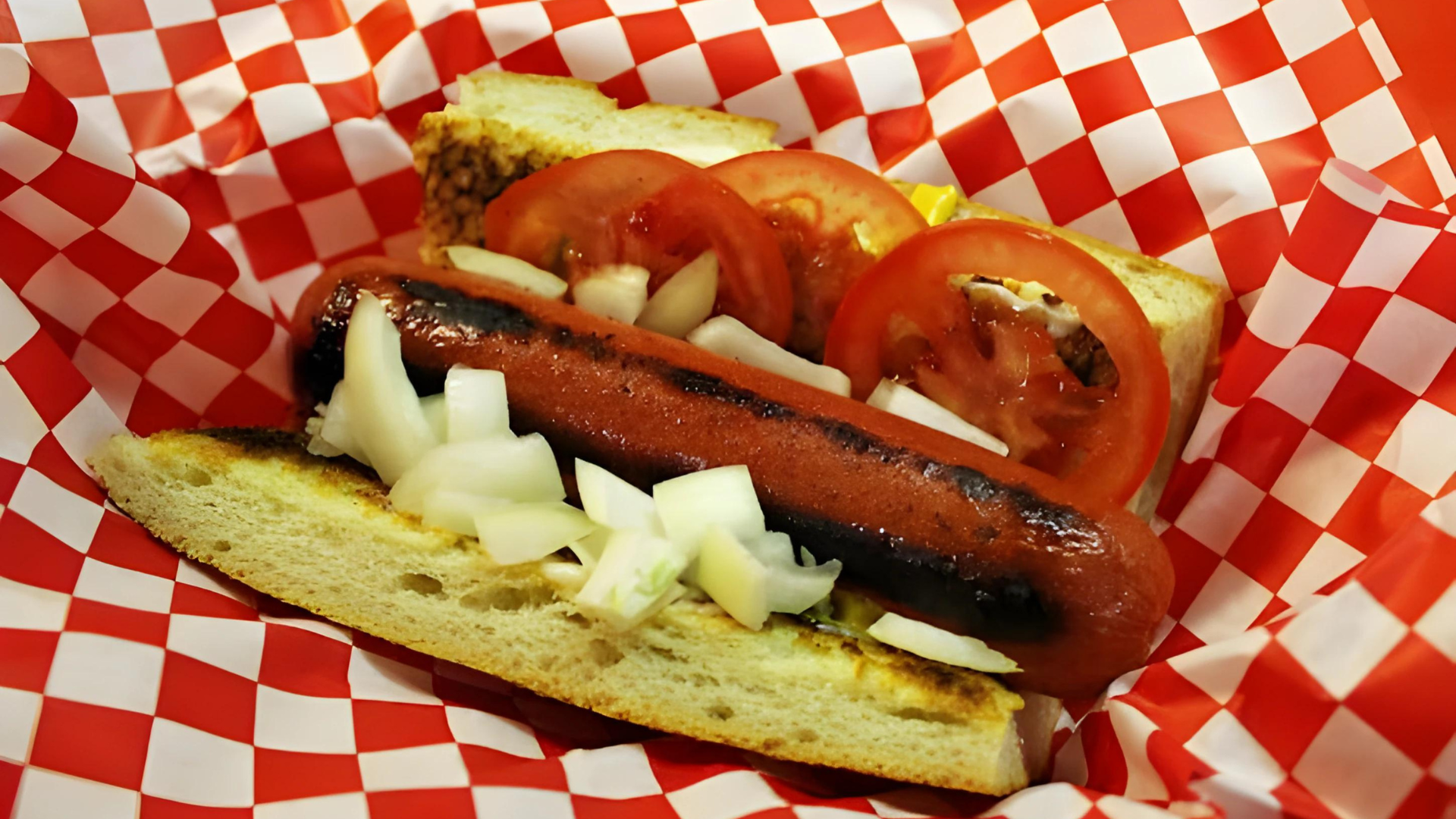 A hot dog with tomatoes and onions on a checkered paper