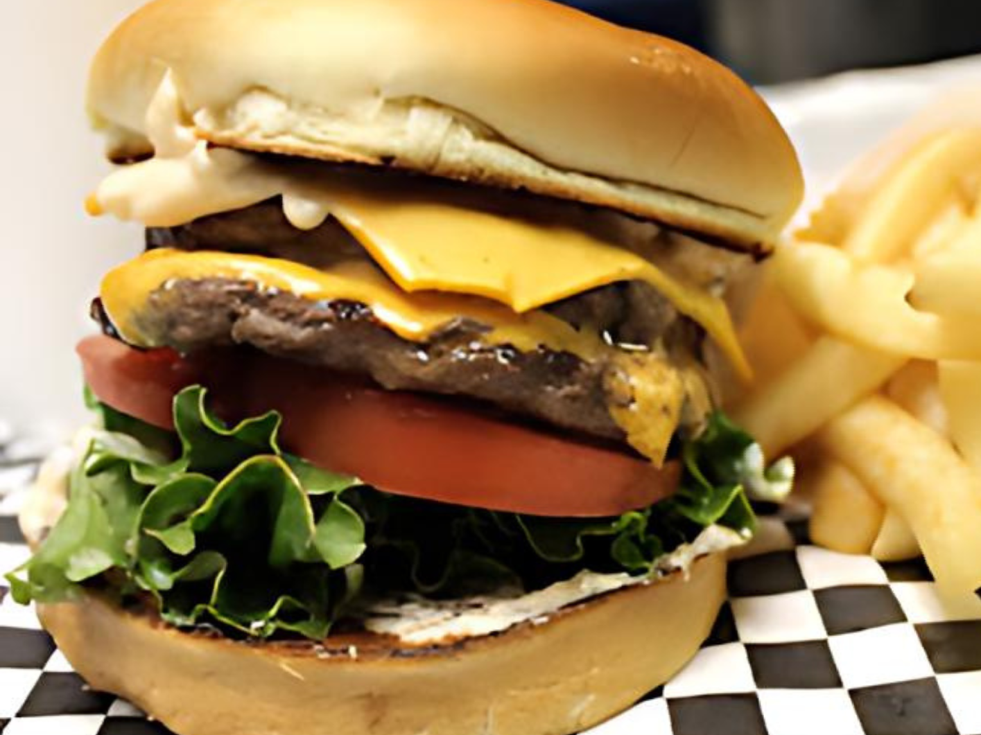 A hamburger and french fries on a checkered napkin on a table.