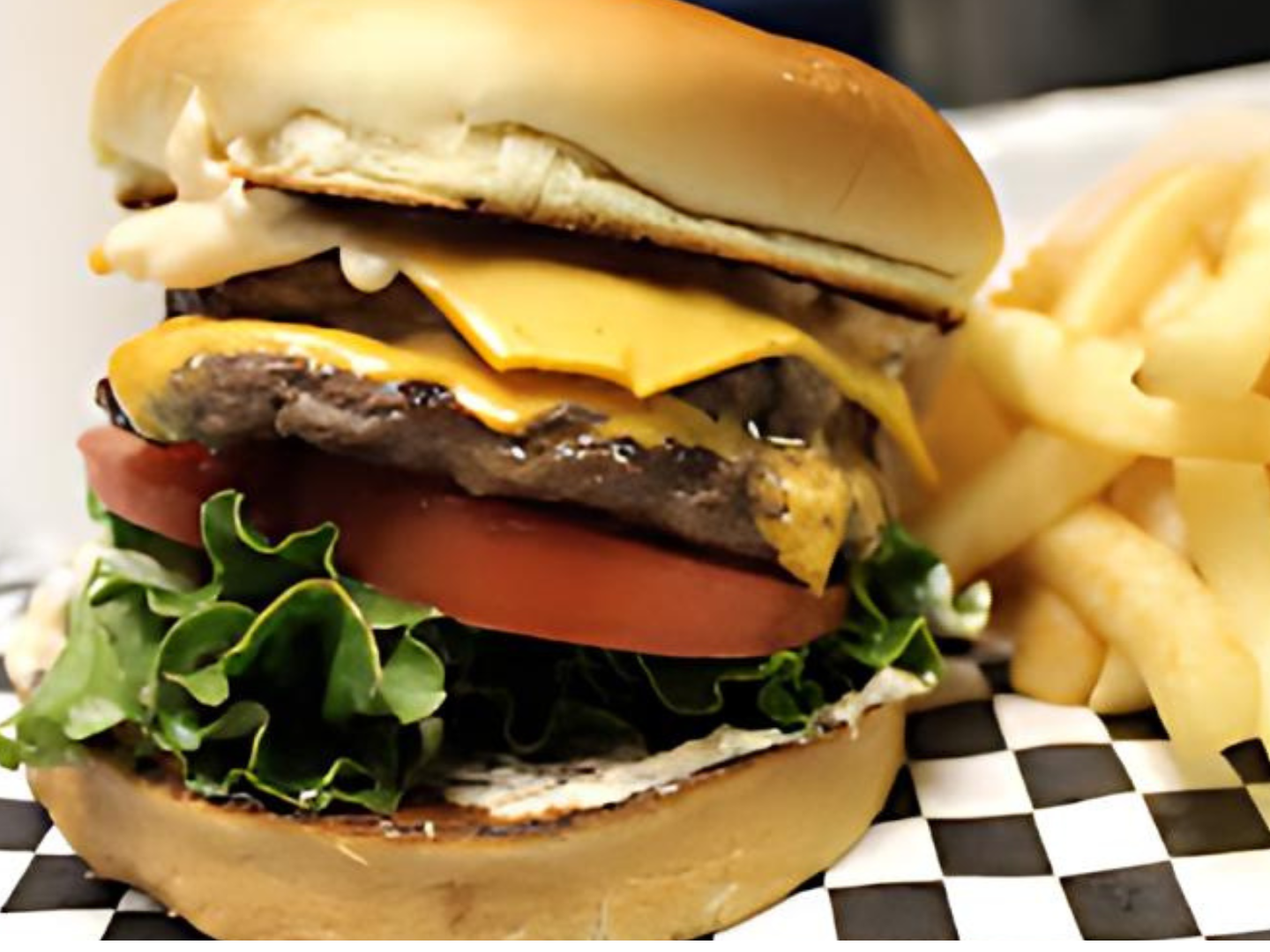 A hamburger and french fries on a checkered napkin on a table.