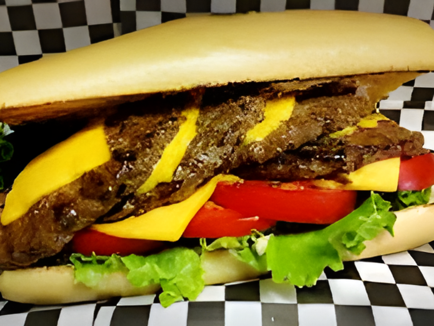 A sandwich with cheese lettuce and tomatoes on a checkered paper