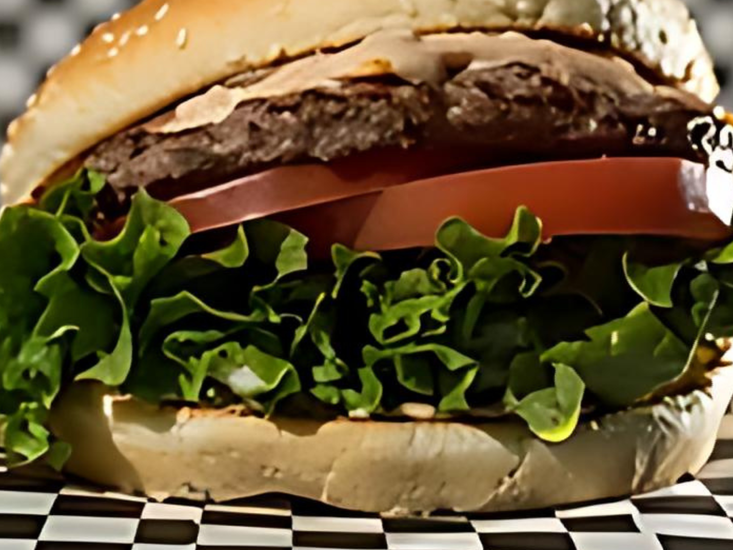 A hamburger with lettuce tomato and cheese on a checkered table cloth