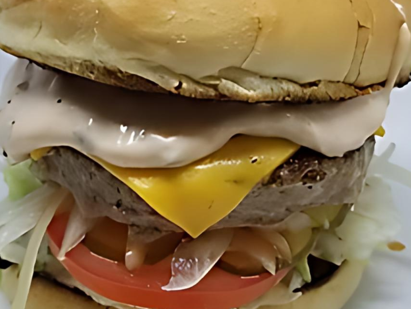 A hamburger with cheese , lettuce , tomato and mayonnaise on a bun.