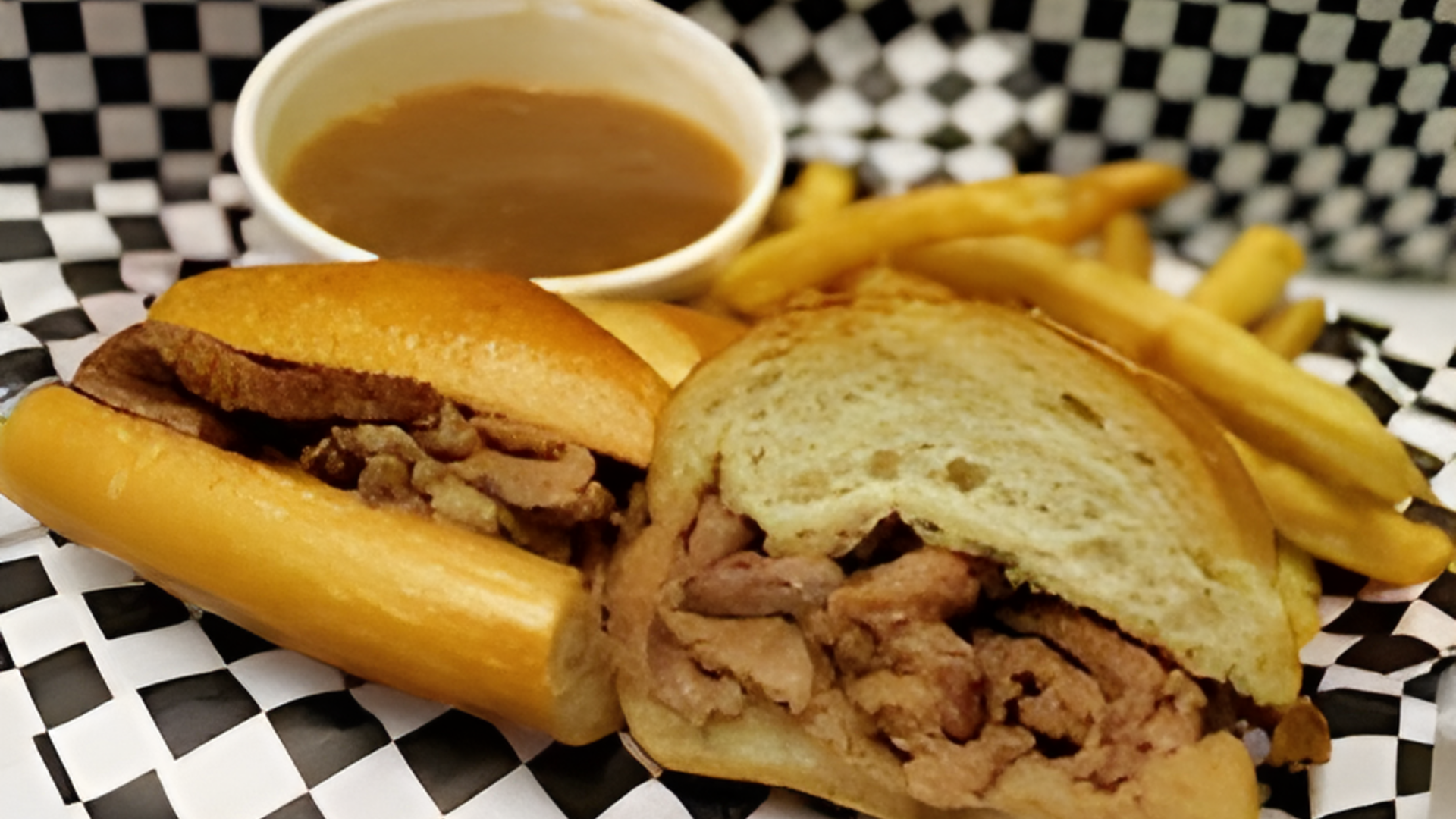 A roast beef sandwich with french fries and gravy on a checkered napkin.