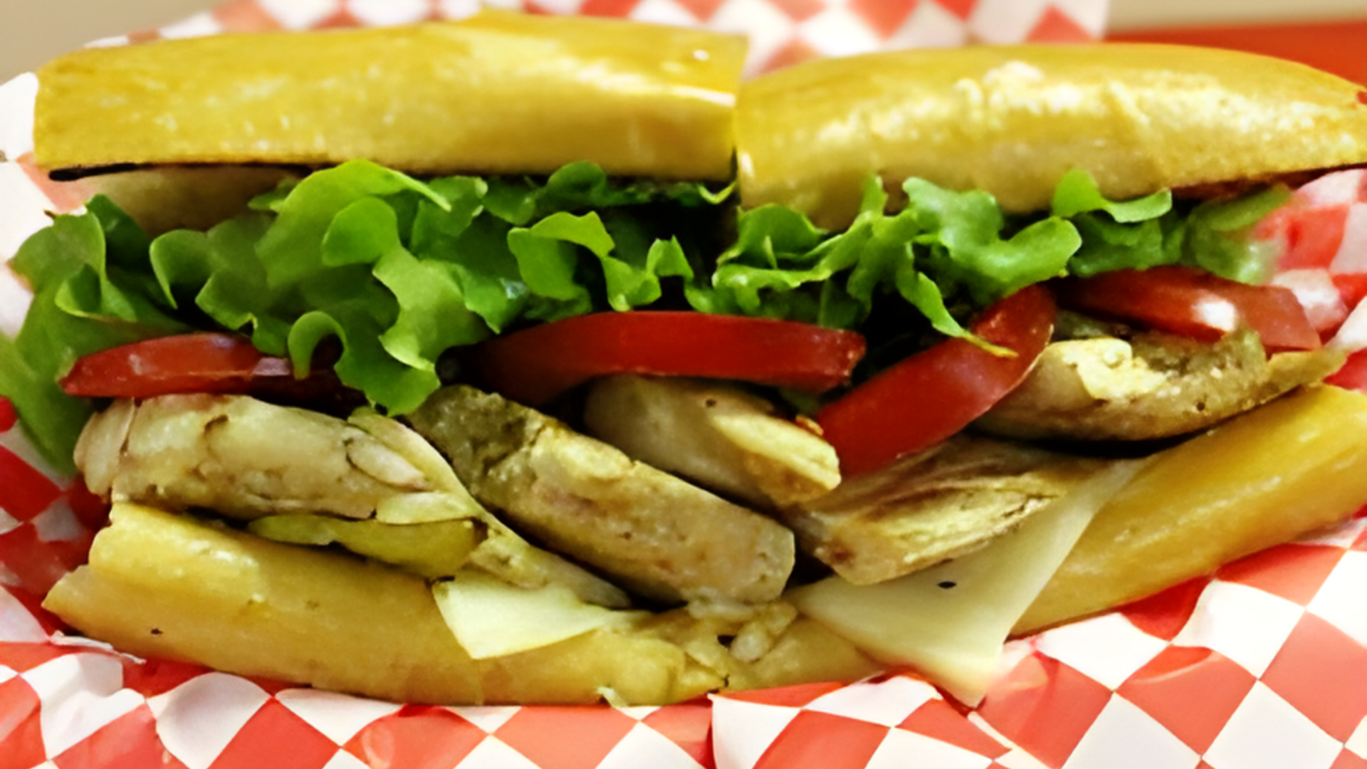 A sub sandwich with chicken lettuce and tomatoes on a checkered paper