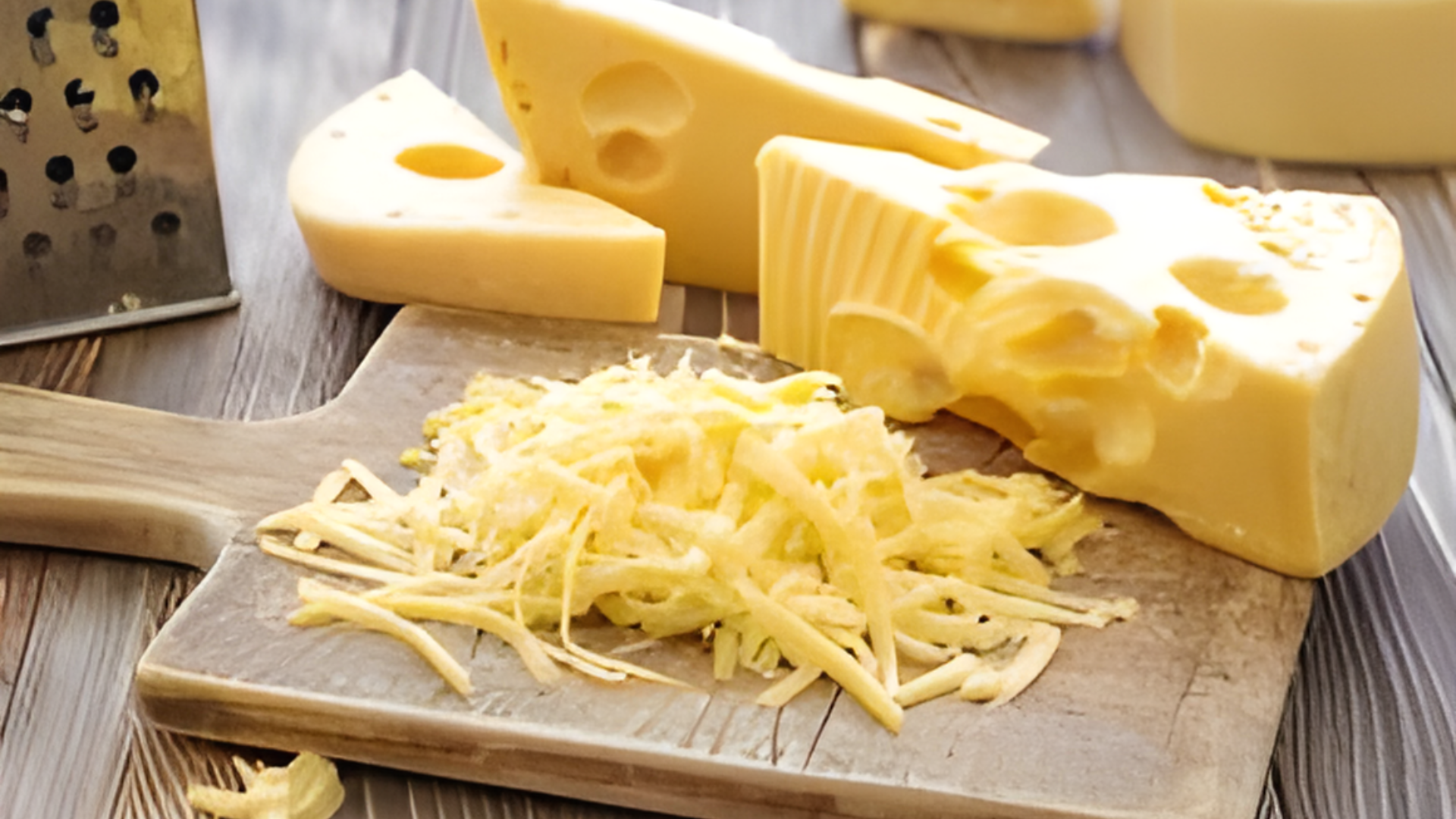 Cheese is being grated on a wooden cutting board.