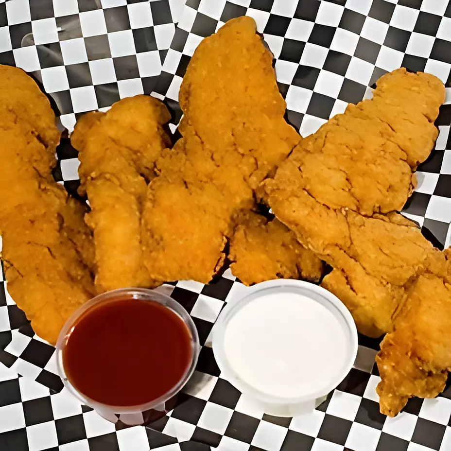 A basket of chicken tenders with a dipping sauce on a checkered paper